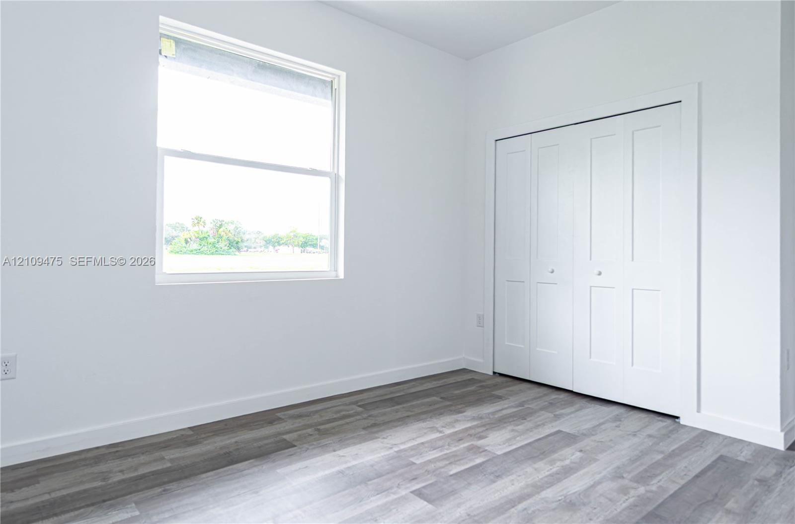 Room featuring wood-finish flooring, a single-hung window, and a built-in four-panel bifold closet door
