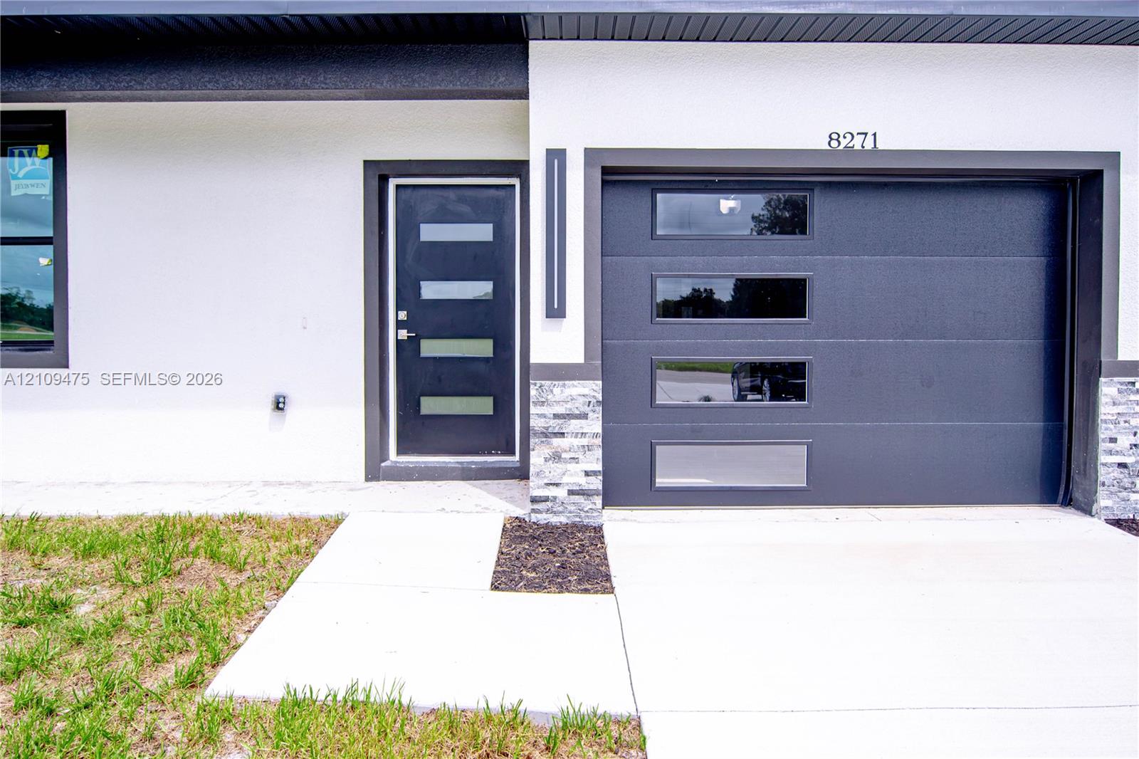 Modern exterior featuring a smooth white stucco facade, a dark metal garage door with horizontal glass panels, a matching entryway door with glass inserts, and stacked stone masonry accents