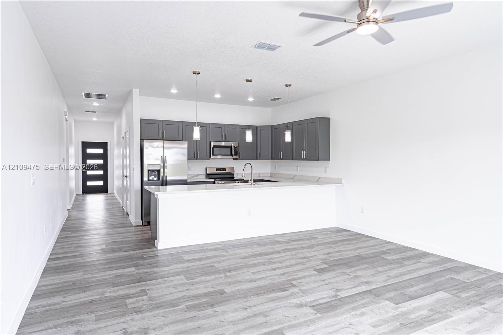 Open kitchen featuring grey cabinetry, quartz countertops, stainless steel appliances, pendant lighting, and wood-finish flooring