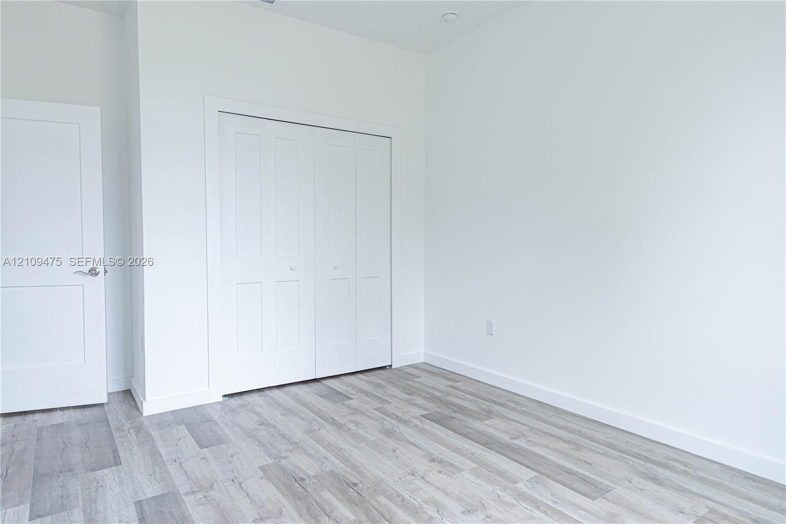 Wood-finish flooring, multi-panel interior door, and four-panel bi-fold closet doors with polished hardware