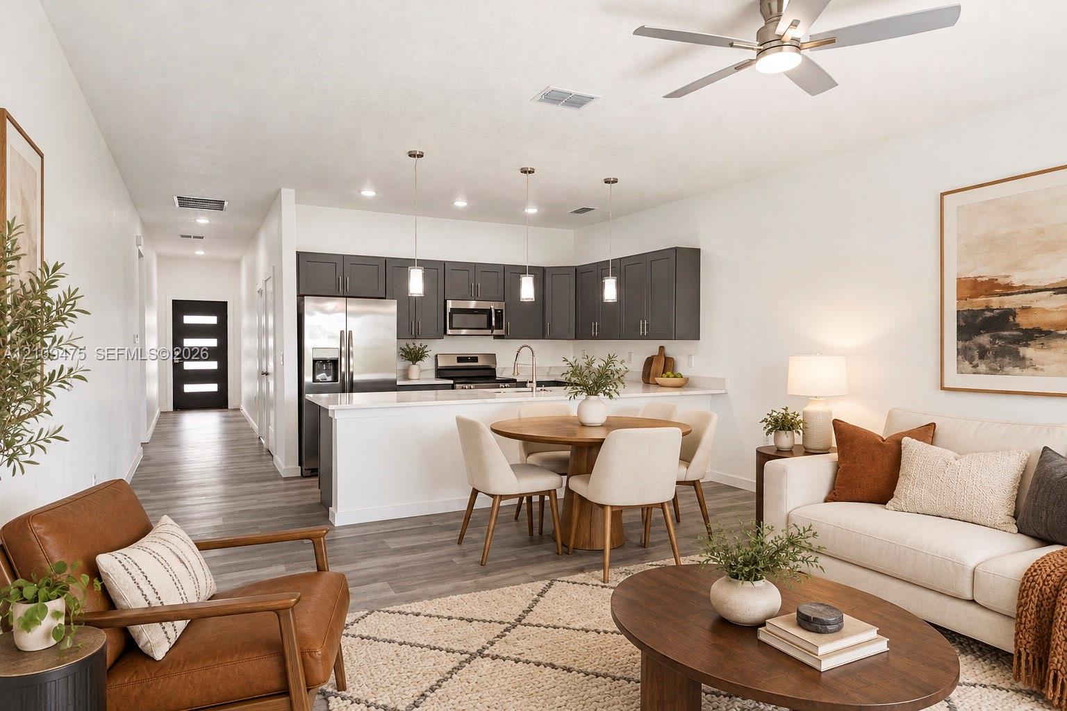 Open-concept kitchen featuring dark cabinetry, quartz countertops, stainless steel appliances, pendant lighting, and wood-finish flooring