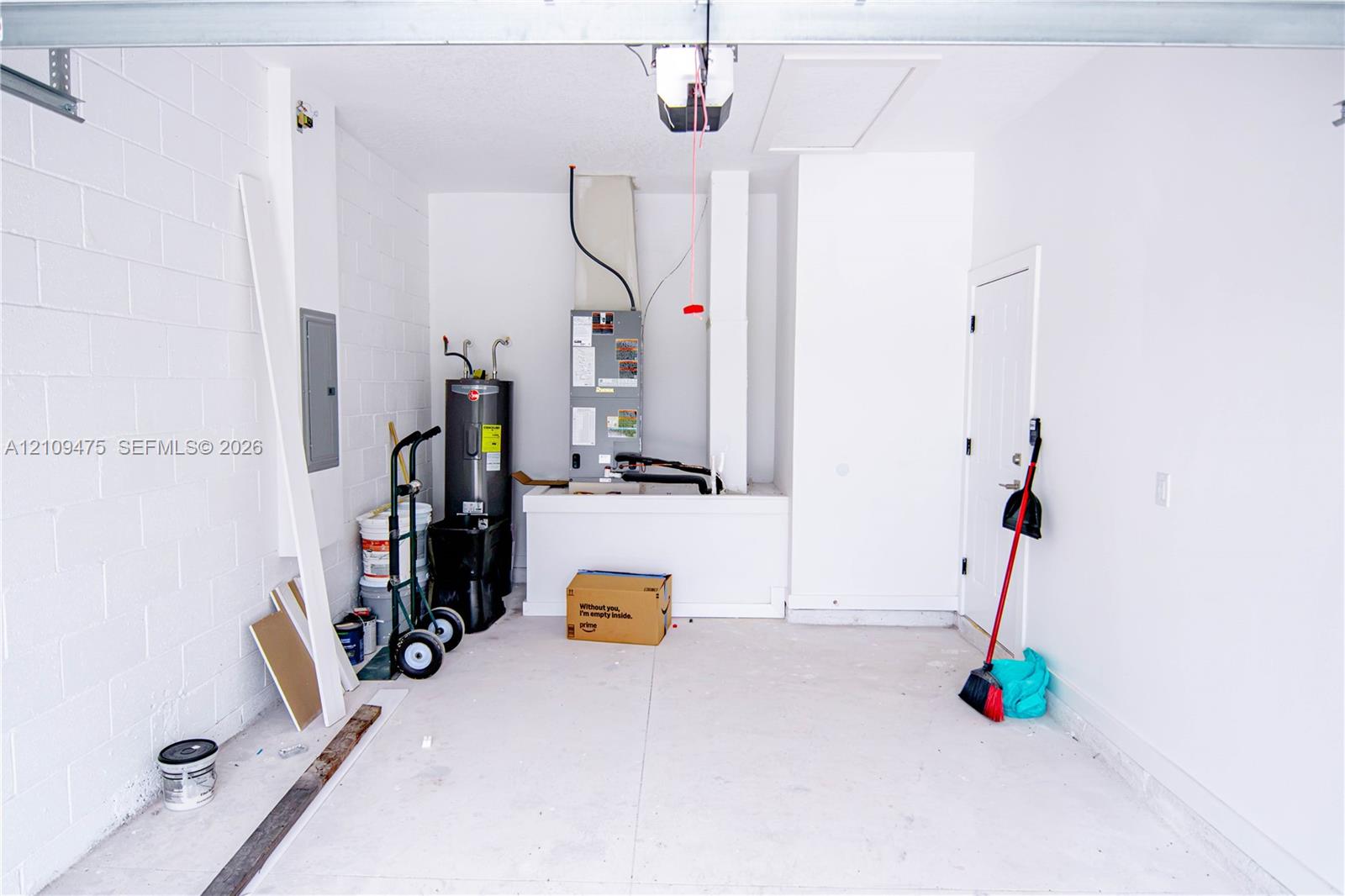 Garage space featuring painted concrete block walls, a concrete floor, an integrated electrical panel, and mechanical systems including a water heater and HVAC unit