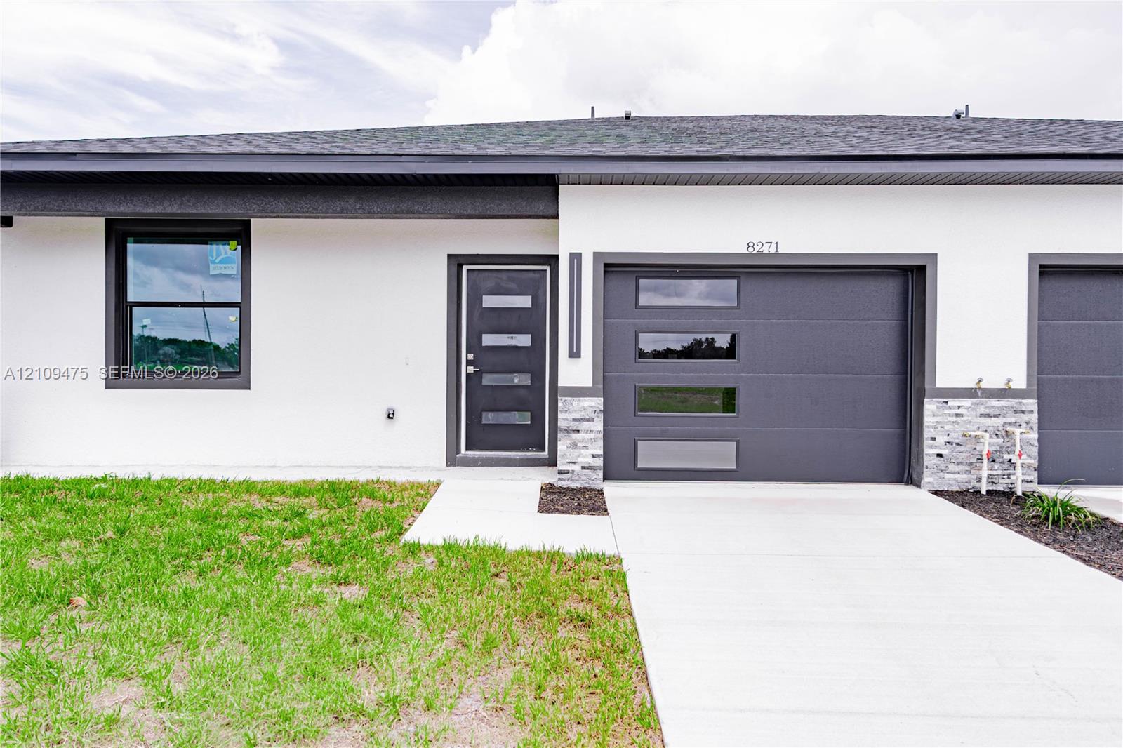 Exterior featuring smooth white stucco siding, contrasting dark-toned trim, a multi-panel front door with horizontal glass insets, a sectional garage door with horizontal glass windows, and stacked stone veneer accents
