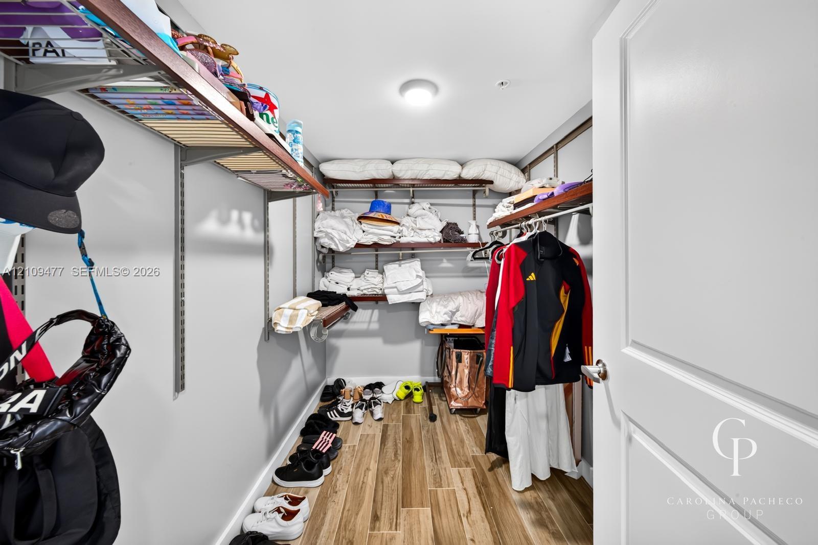 Storage space featuring wood-finish flooring, adjustable metal shelving, and a flush-mount ceiling light fixture