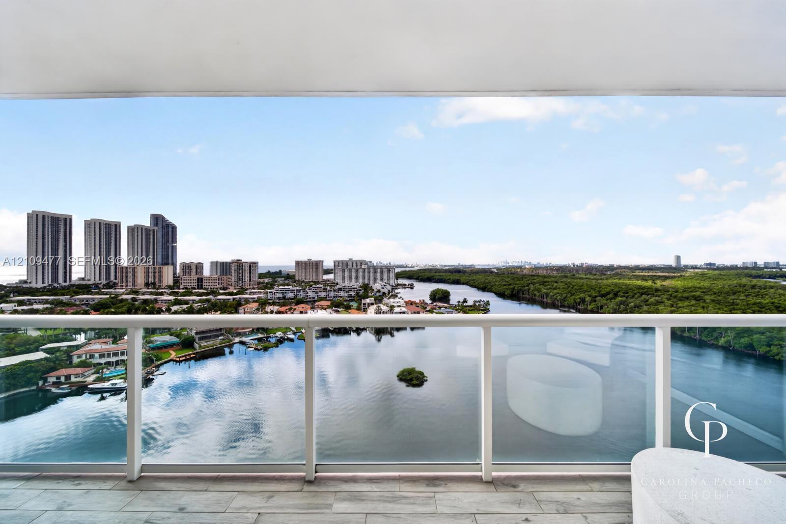 Covered balcony featuring wood-finish flooring and a minimalist glass panel railing with a water and city skyline backdrop