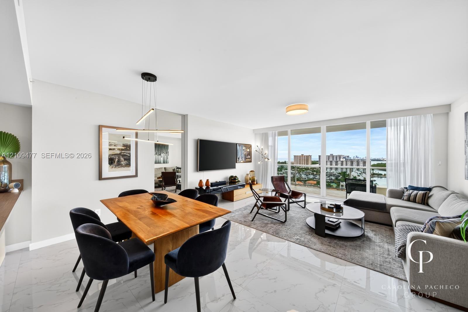 Open-concept interior featuring large-format tile flooring, expansive floor-to-ceiling glass windows, linear pendant lighting, and a private balcony