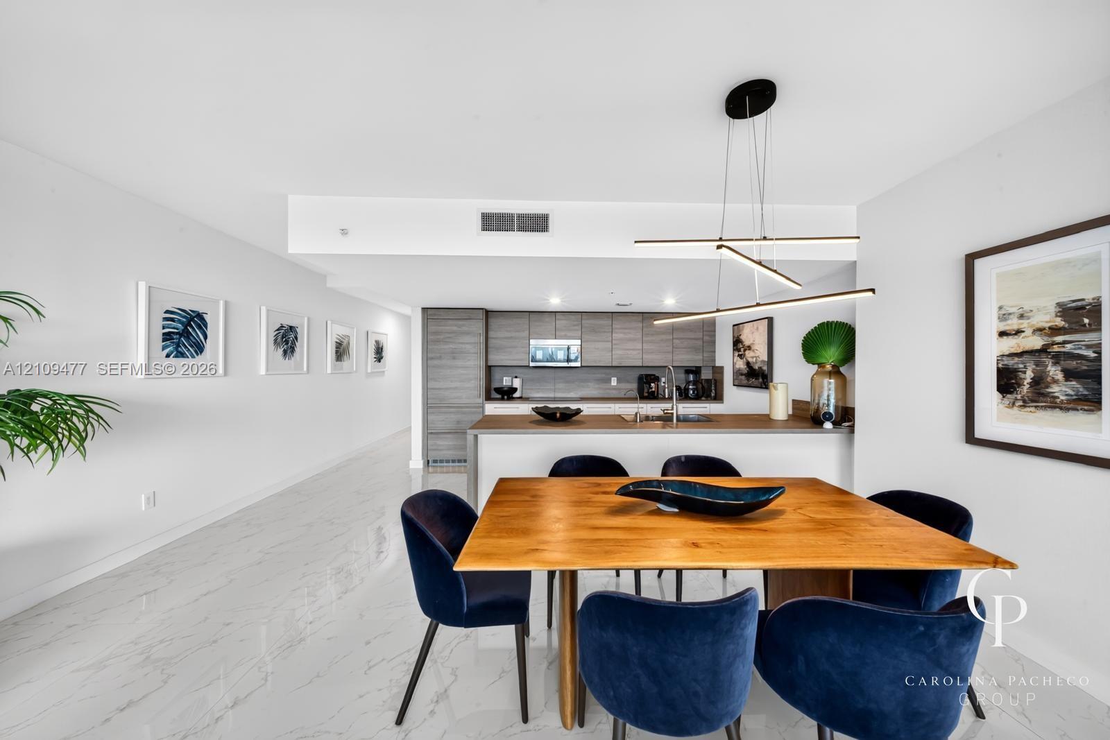 Modern kitchen featuring grey-toned cabinetry, a spacious peninsula, integrated stainless steel appliances, polished stone-finish flooring, and a contemporary linear pendant light fixture