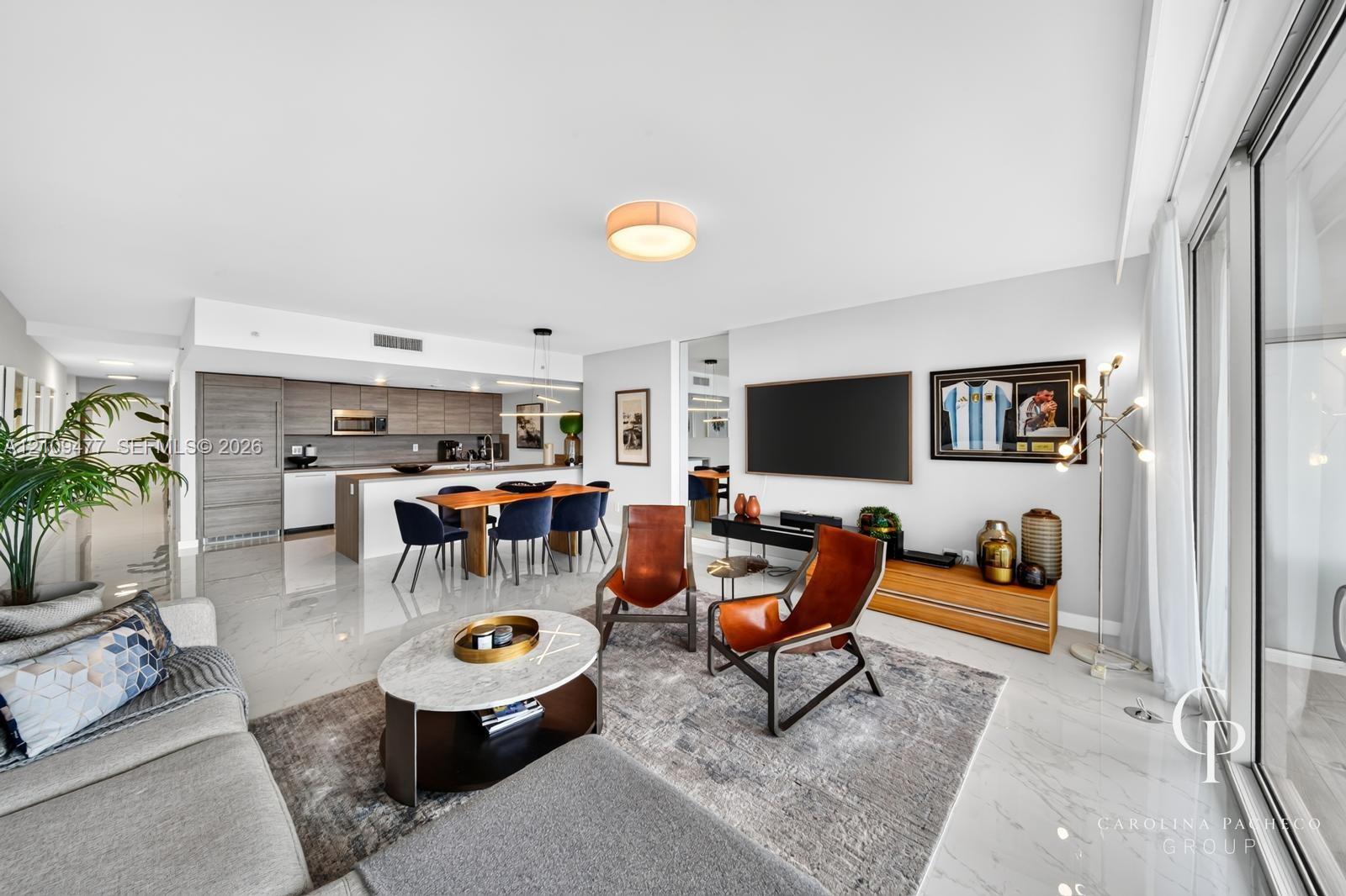 Open-concept interior featuring light-toned flooring, modern kitchen cabinetry with a central island, recessed lighting, and floor-to-ceiling glass sliding doors