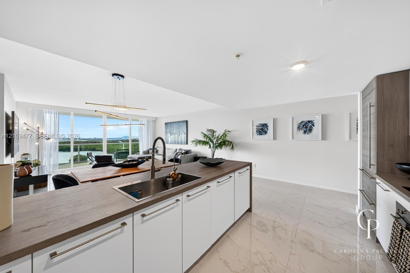 Kitchen featuring a central island with a wood-finish countertop, stainless steel undermount sink, high-arc faucet, white cabinetry with horizontal hardware, and large-format tile flooring
