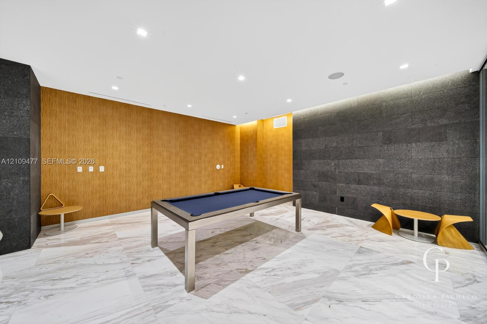Interior space featuring large-format stone floor tiles, natural wood-finish wall paneling, charcoal-toned stone feature walls, and recessed ceiling lighting