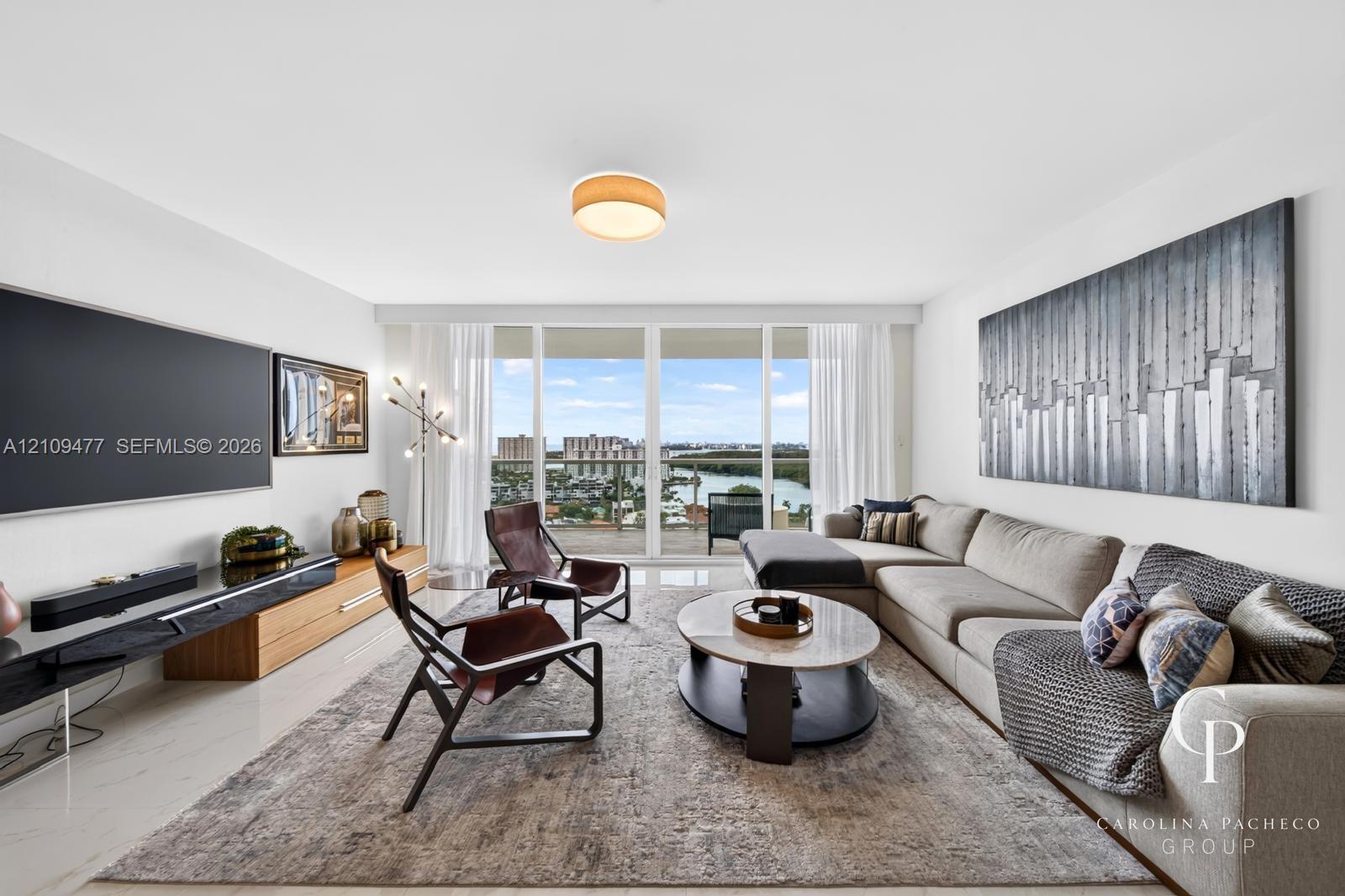 Living area featuring floor-to-ceiling glass doors, neutral tile flooring, flush-mount lighting, and exterior access to a balcony with water scenery