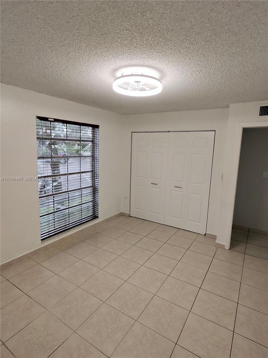 Neutral tile flooring, circular flush-mount LED ceiling fixture, dual-panel closet doors, and a window with horizontal blinds