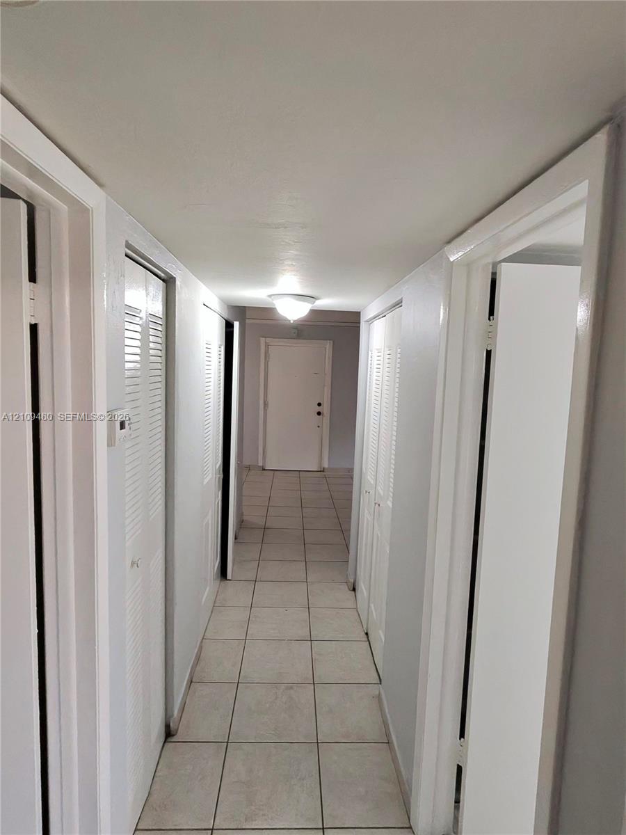 Neutral-toned tile flooring, multiple louvered-door closets, and a flush-mount ceiling fixture
