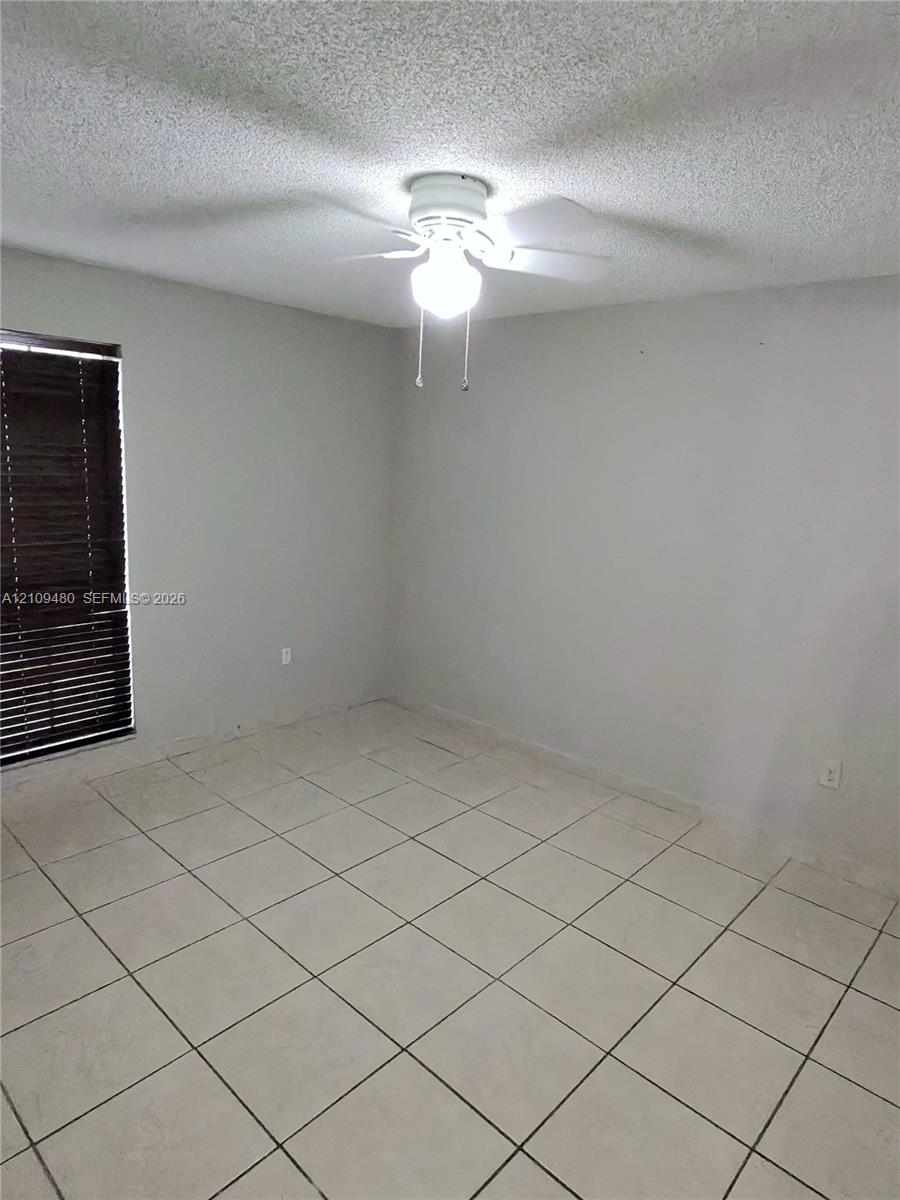 Neutral-toned interior room featuring light-colored tile flooring, a ceiling-mounted light fixture with a fan, and a window with horizontal slatted blinds