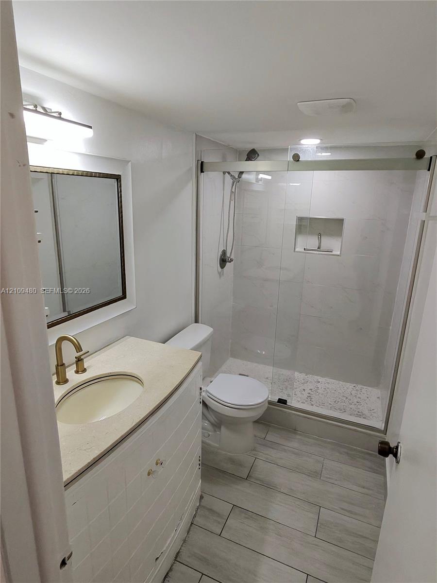 Bathroom featuring a white vanity with a light-toned countertop, a shower with sliding glass doors and an integrated niche, wood-finish floor tile, and gold-tone hardware