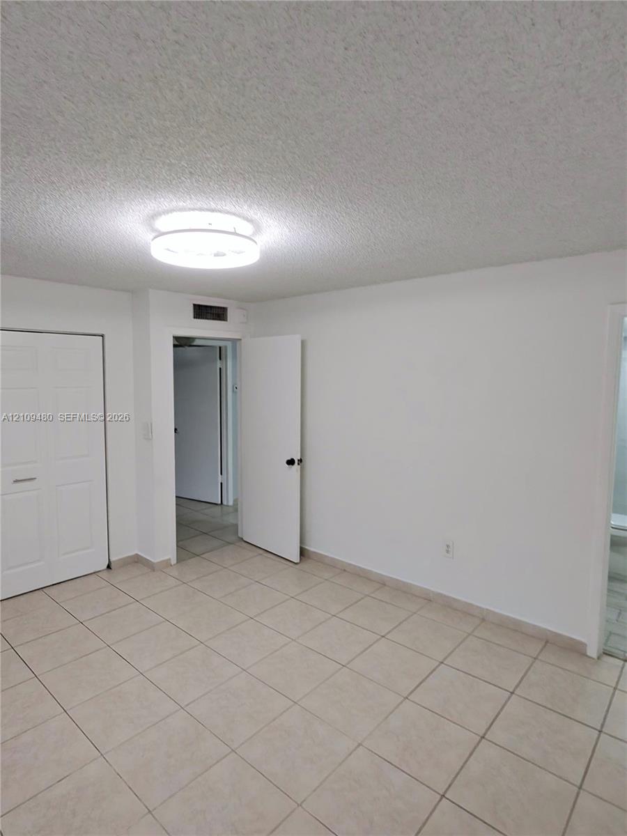 Neutral tile flooring, textured ceiling, flush-mount circular lighting, and paneled closet doors