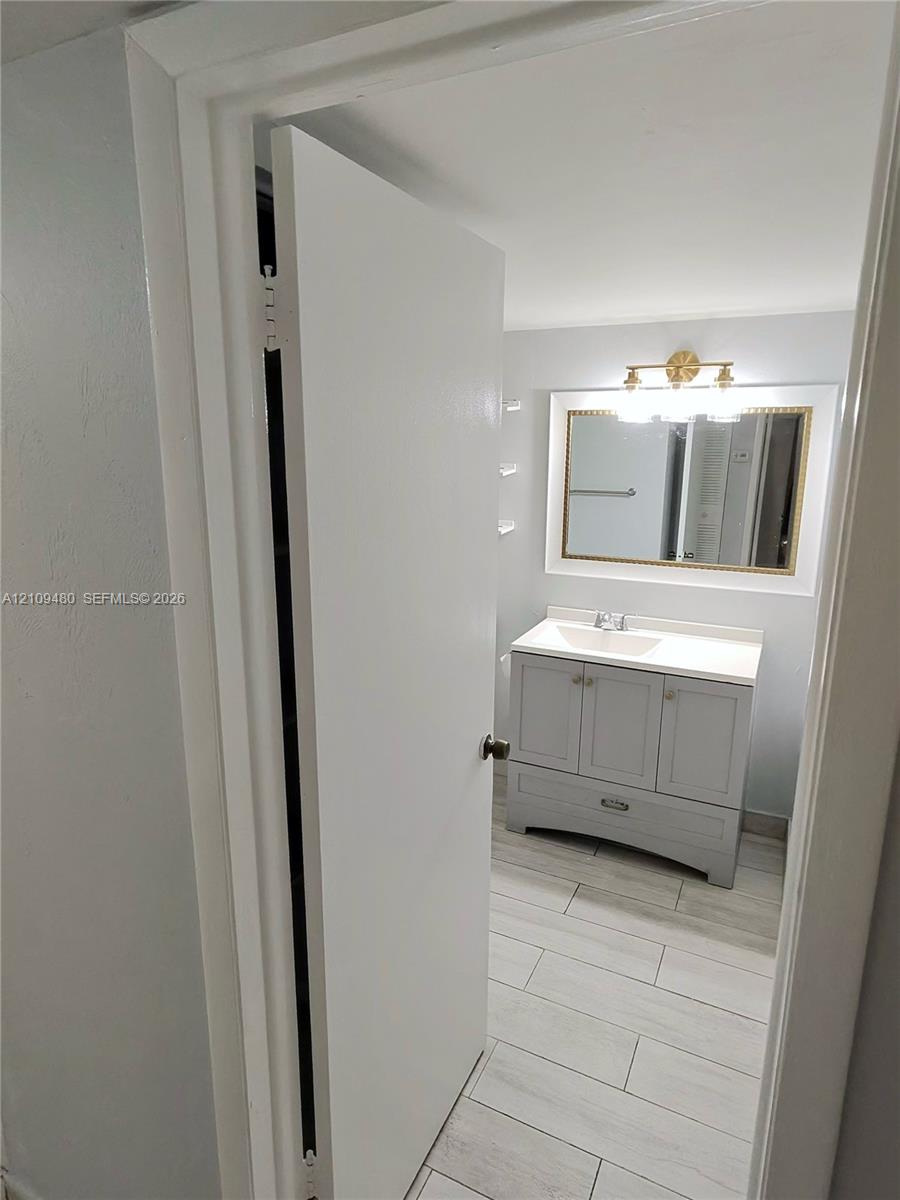 Bathroom featuring a grey vanity with a rectangular sink, stone-finish countertop, framed wall mirror, multi-bulb vanity light, and light-toned tile flooring
