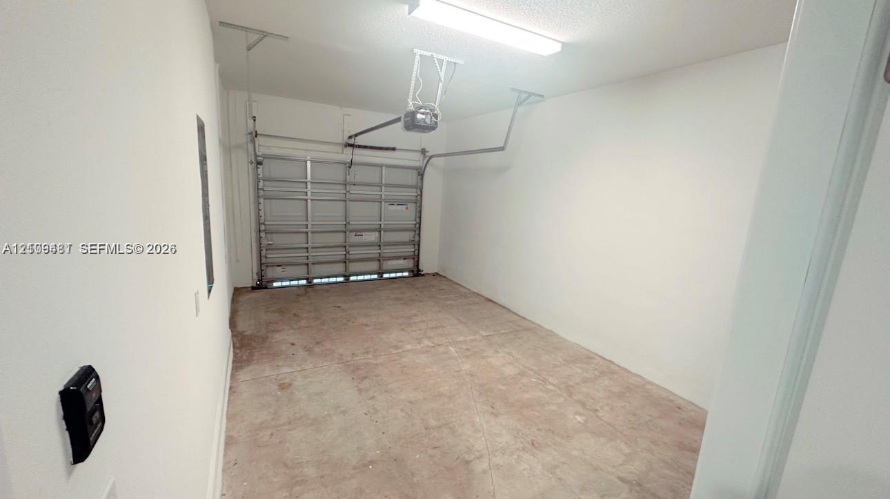 Enclosed single-car garage featuring a roll-up door, automatic overhead opener, fluorescent lighting, and concrete flooring