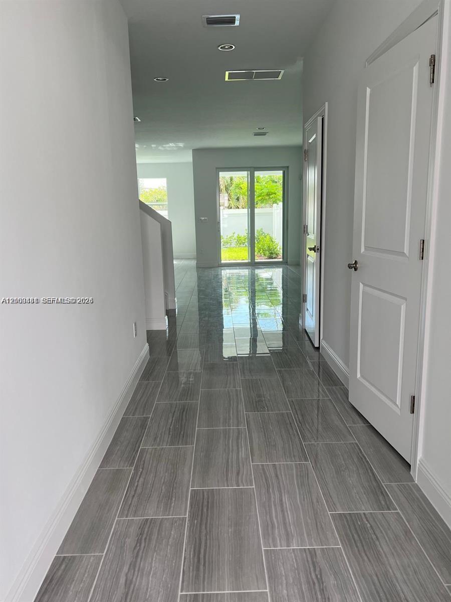 Interior hallway featuring grey-toned wood-finish tile flooring, recessed ceiling lighting, and crisp white-painted walls