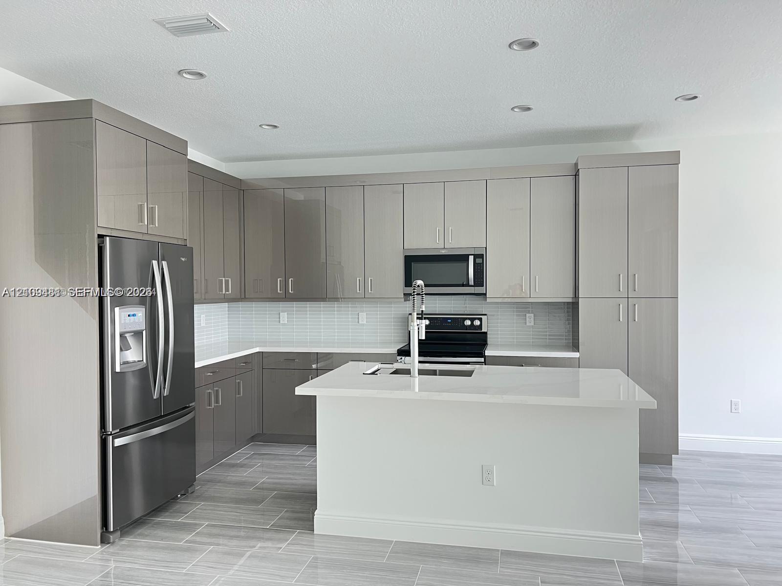 Kitchen featuring high-gloss cabinetry, stone-finish countertops, stainless steel appliances, a central island with a built-in sink, and tile flooring