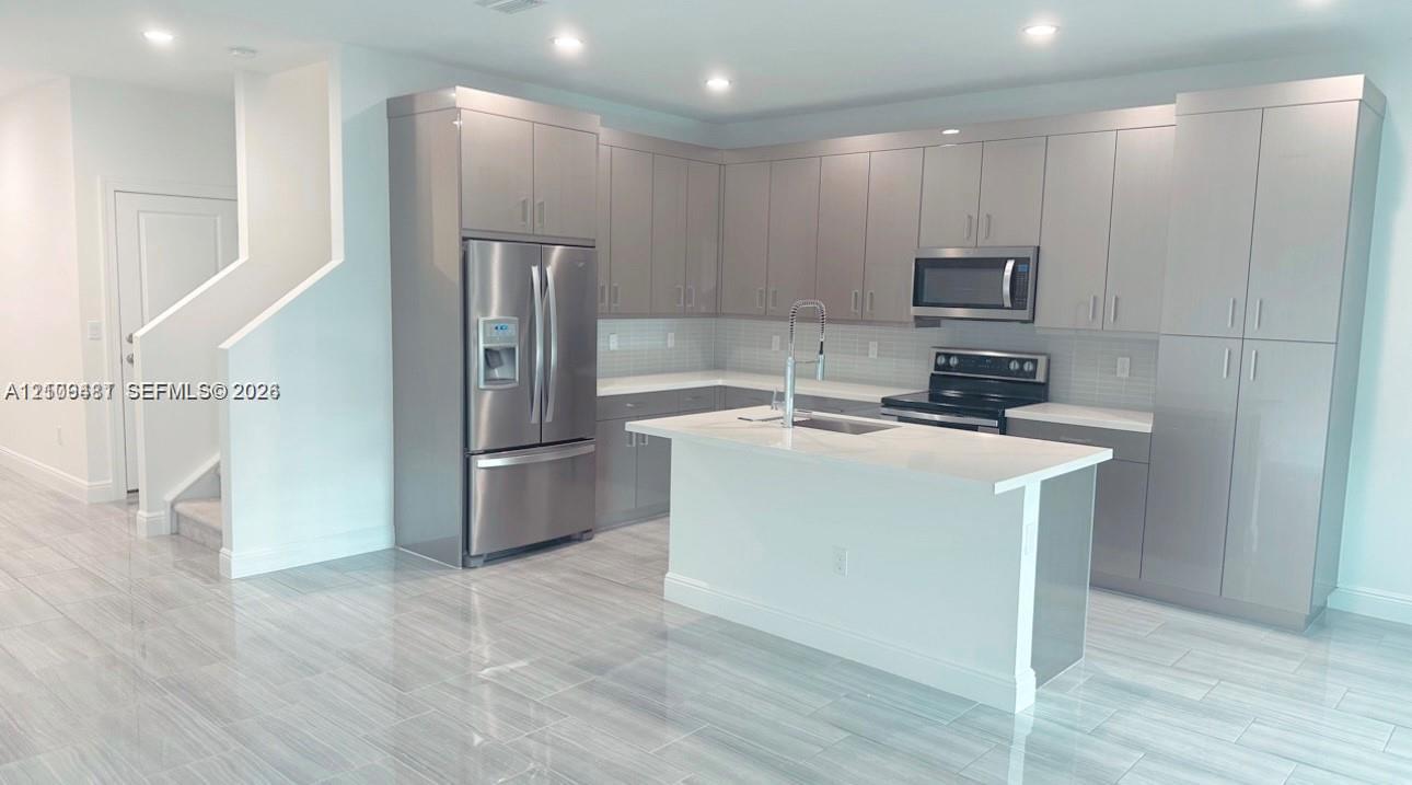 Kitchen featuring flat-panel cabinetry, a central island with a stone-surface countertop, stainless steel appliances, and large-format tile flooring