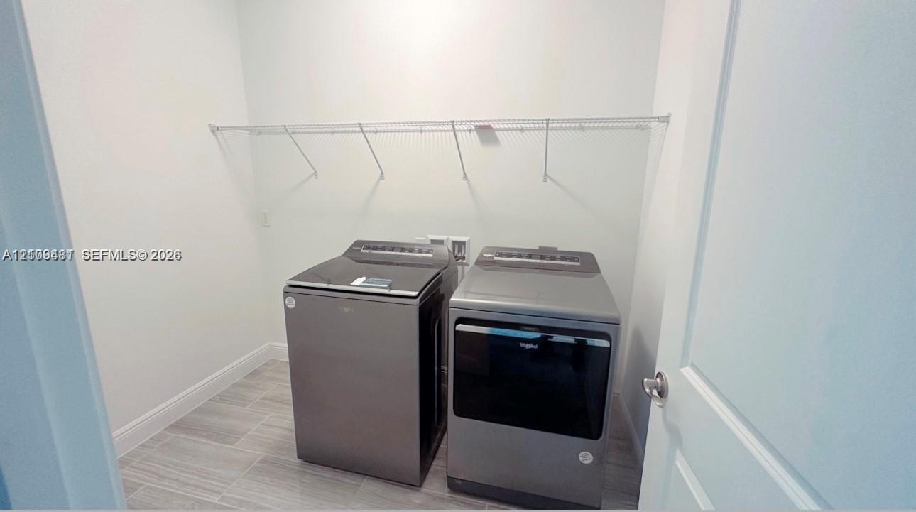 Laundry area featuring grey tile flooring, wall-mounted wire shelving, and built-in washing machine and dryer