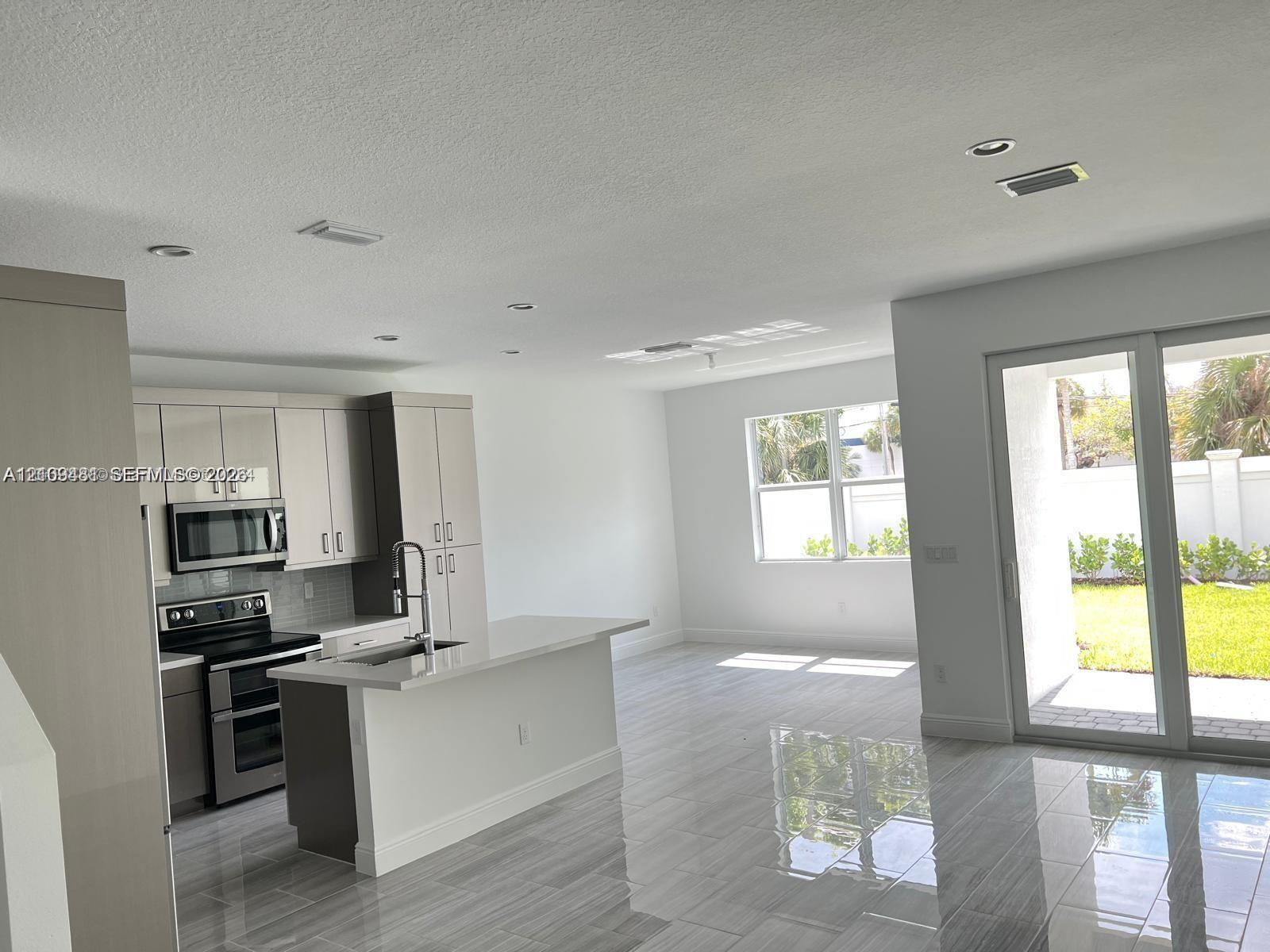 Kitchen featuring flat-panel cabinetry, quartz countertops, a kitchen island with a built-in sink, stainless steel appliances, and large-format porcelain tile flooring