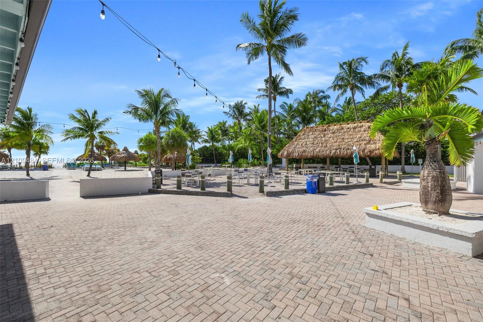 Outdoor space featuring a herringbone-patterned brick paver patio, thatched-roof tiki hut, built-in concrete planters, and perimeter string lighting