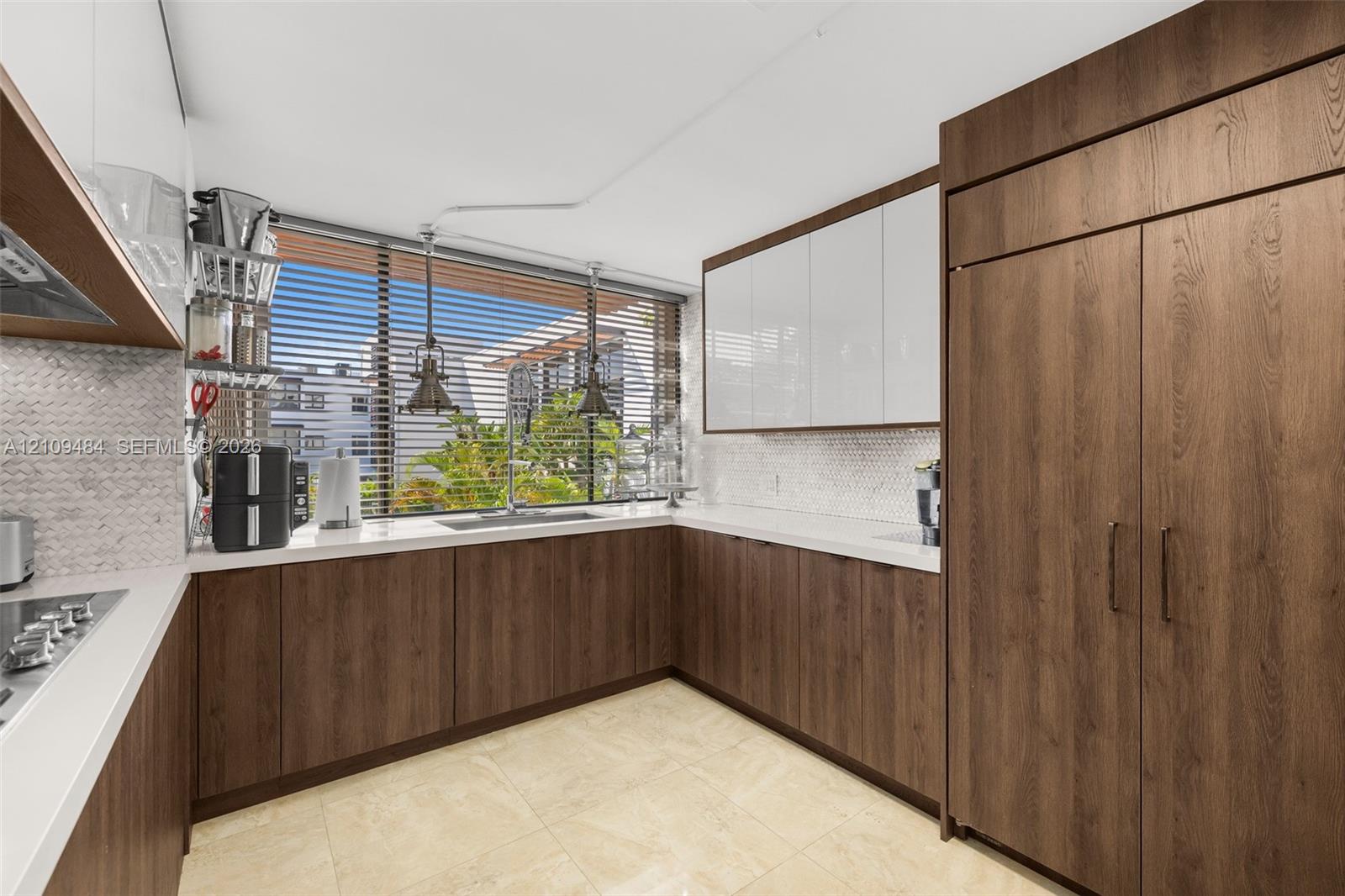 Kitchen featuring two-tone cabinetry with wood-finish lower units and high-gloss white upper cabinets, light-toned stone countertops, hexagonal mosaic tile backsplash, and integrated refrigeration