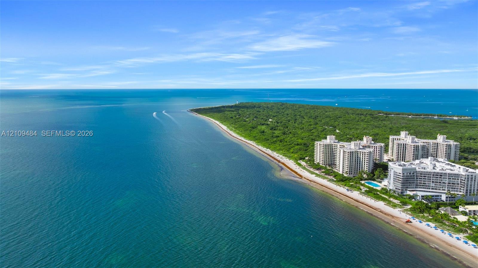 Aerial perspective of coastal multi-story residential buildings featuring immediate proximity to the shoreline and direct access to expansive sandy beach frontage