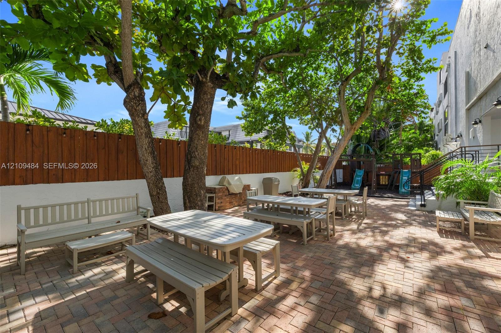 Outdoor patio featuring herringbone-pattern brick paving, vertical wood-plank perimeter fencing, and mature trees