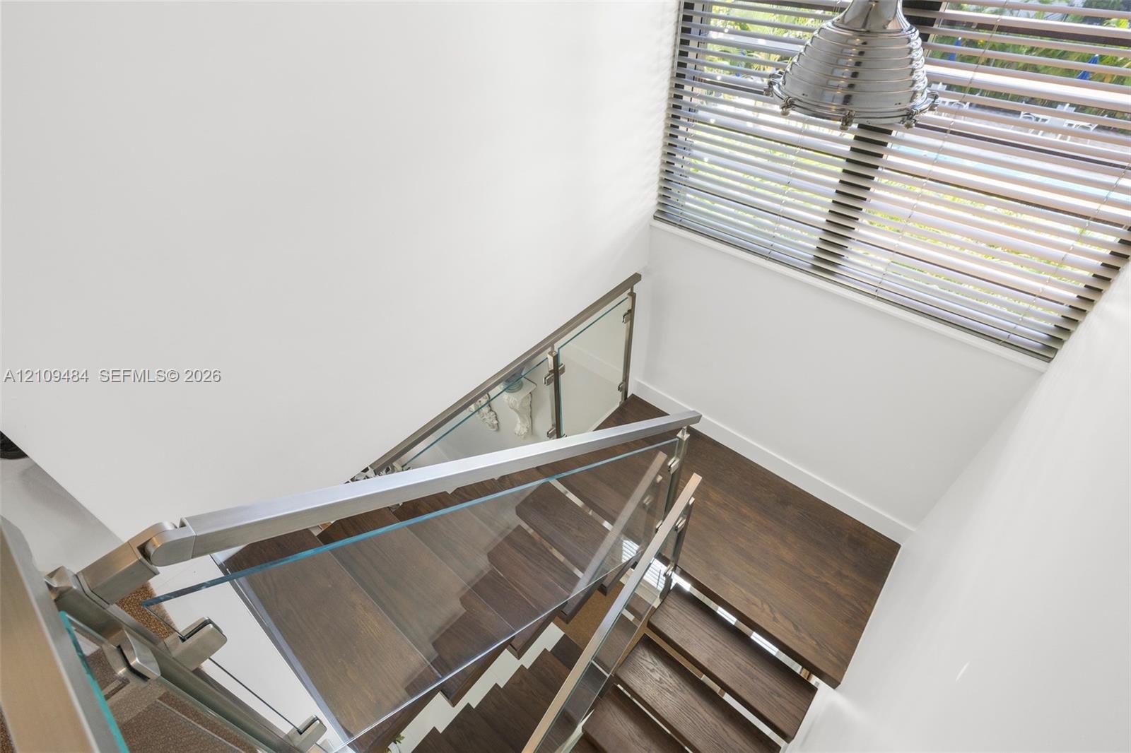 Staircase featuring wood-finish treads, glass panel railing, metallic handrails, and a modern industrial-style pendant light