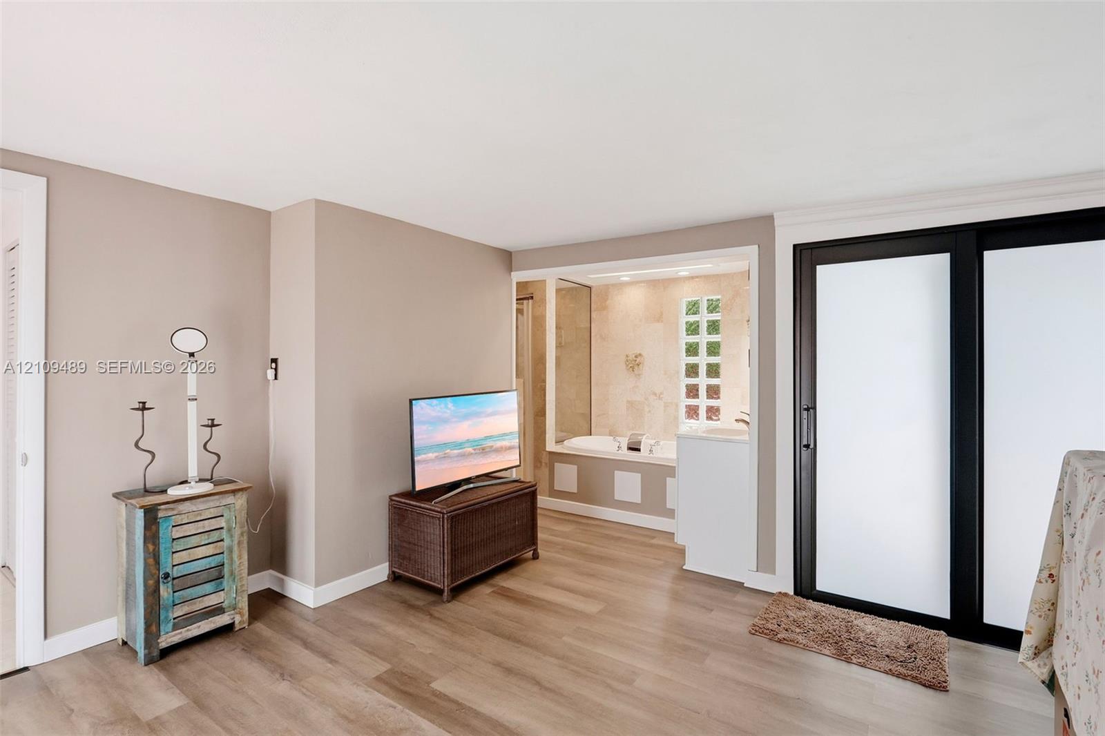 Neutral-toned interior featuring wood-finish flooring, sliding glass doors with dark frames, and a soaking tub alcove accented with natural stone-finish wall tile