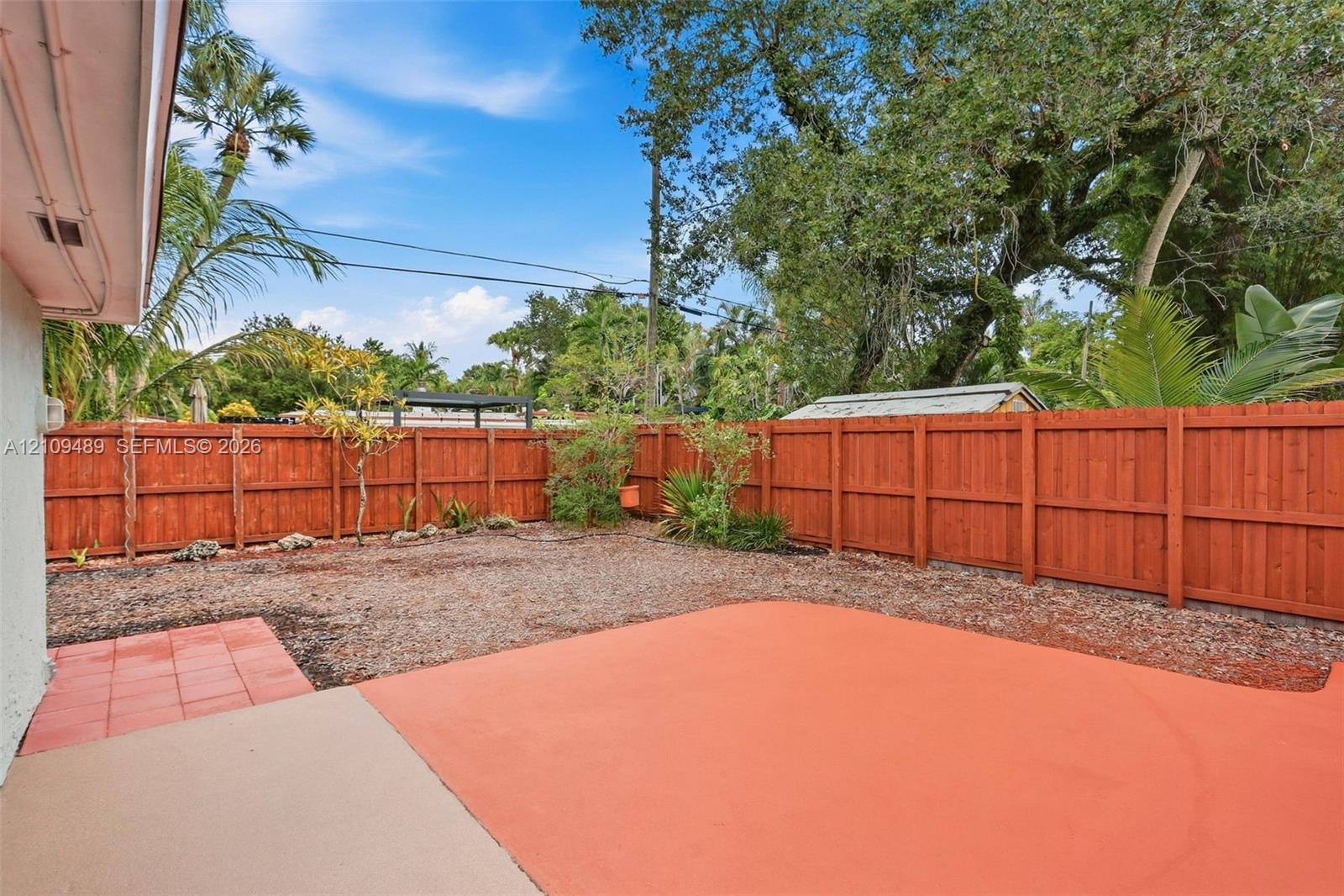 Fenced backyard featuring a painted concrete patio, tiled accent area, and mature landscaping