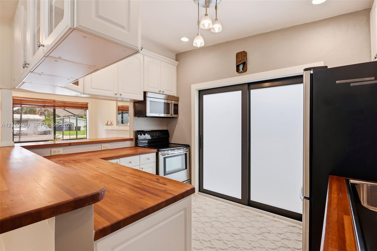 Kitchen featuring white cabinetry, butcher-block countertops, stainless steel appliances, a multi-light pendant fixture, and sliding glass doors