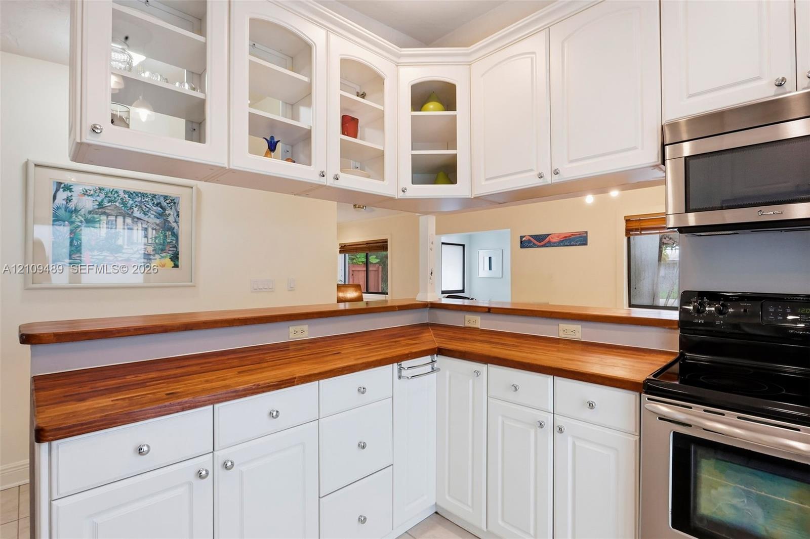 Kitchen featuring white cabinetry with glass-front uppers, natural wood-finish countertops, and stainless steel appliances