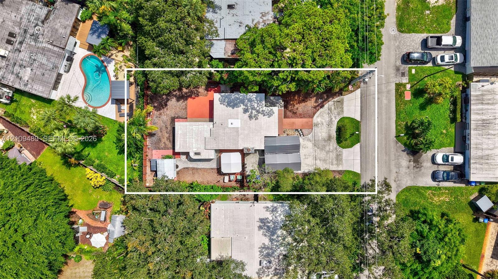 Aerial perspective of a property featuring a multi-section roofline, paved driveway, dedicated parking area, and mature landscaping