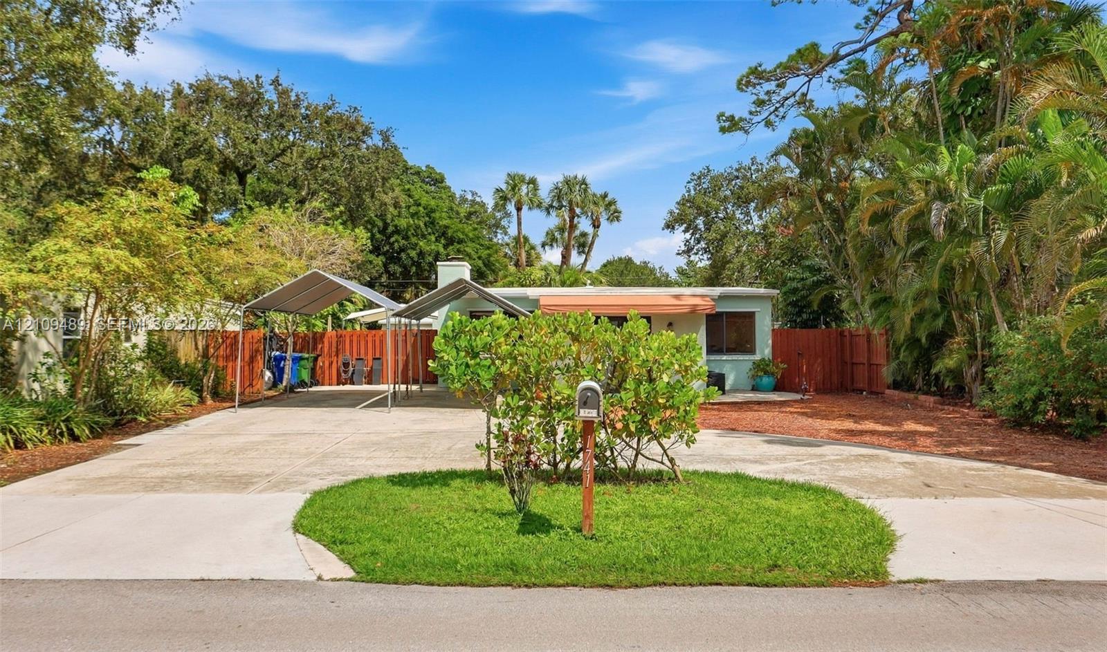 Exterior featuring a concrete driveway, dual metal carports, a landscaped front lawn, and wood privacy fencing