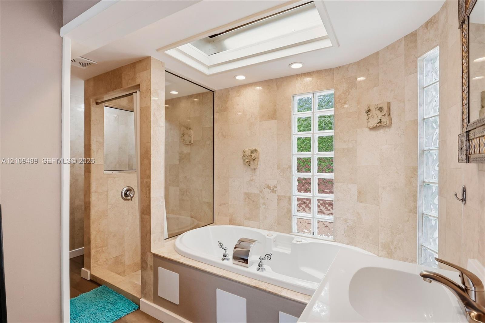Bathroom featuring a drop-in soaking tub, tile-surround shower with a glass partition, dual glass-block windows, and a built-in skylight