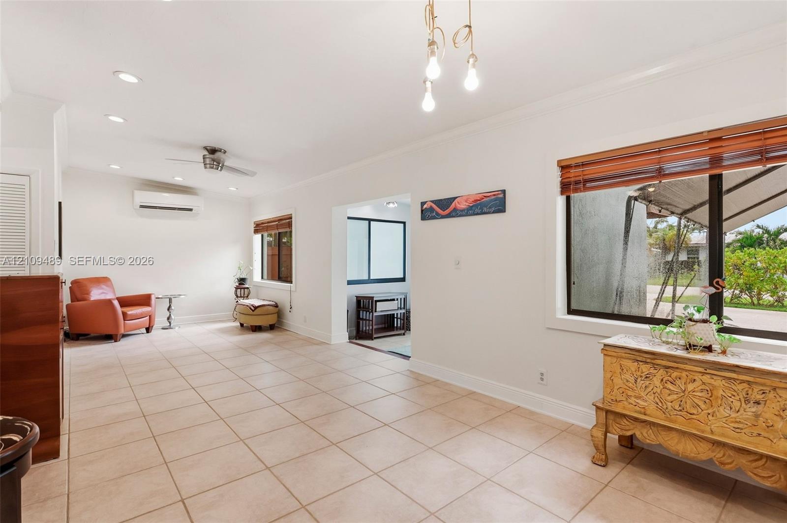 Tile flooring, recessed lighting, wall-mounted climate control unit, crown molding, and large-paned windows with wood-slat blinds
