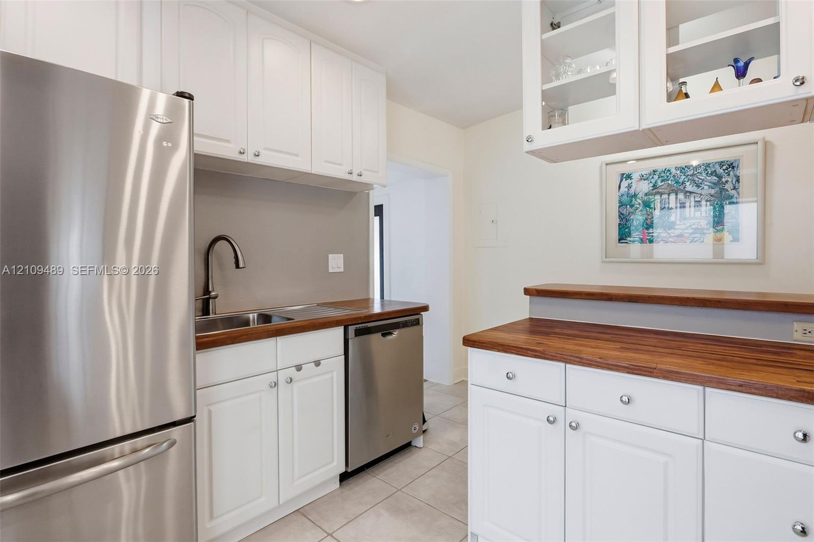 Kitchen featuring white shaker-style cabinetry, wood-finish countertops, stainless steel appliances, a high-arc faucet, and upper glass-front display cabinets