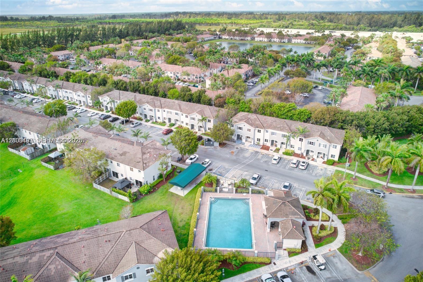 Aerial perspective of a multi-unit residential complex featuring a community swimming pool, paver deck, covered poolside structure, and expansive manicured green space