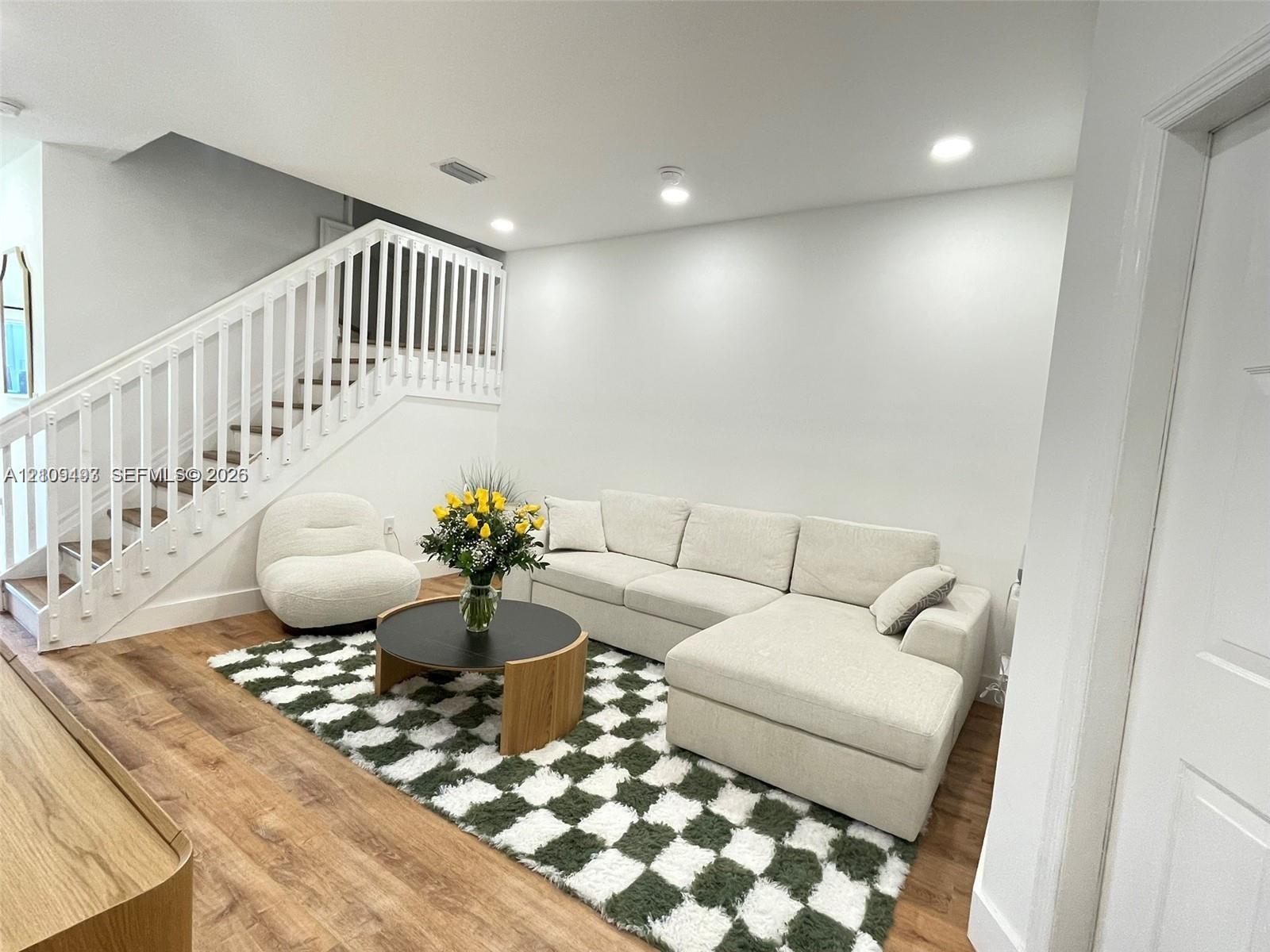 Staircase featuring a white balustrade and wood-finish flooring, complemented by recessed ceiling lighting