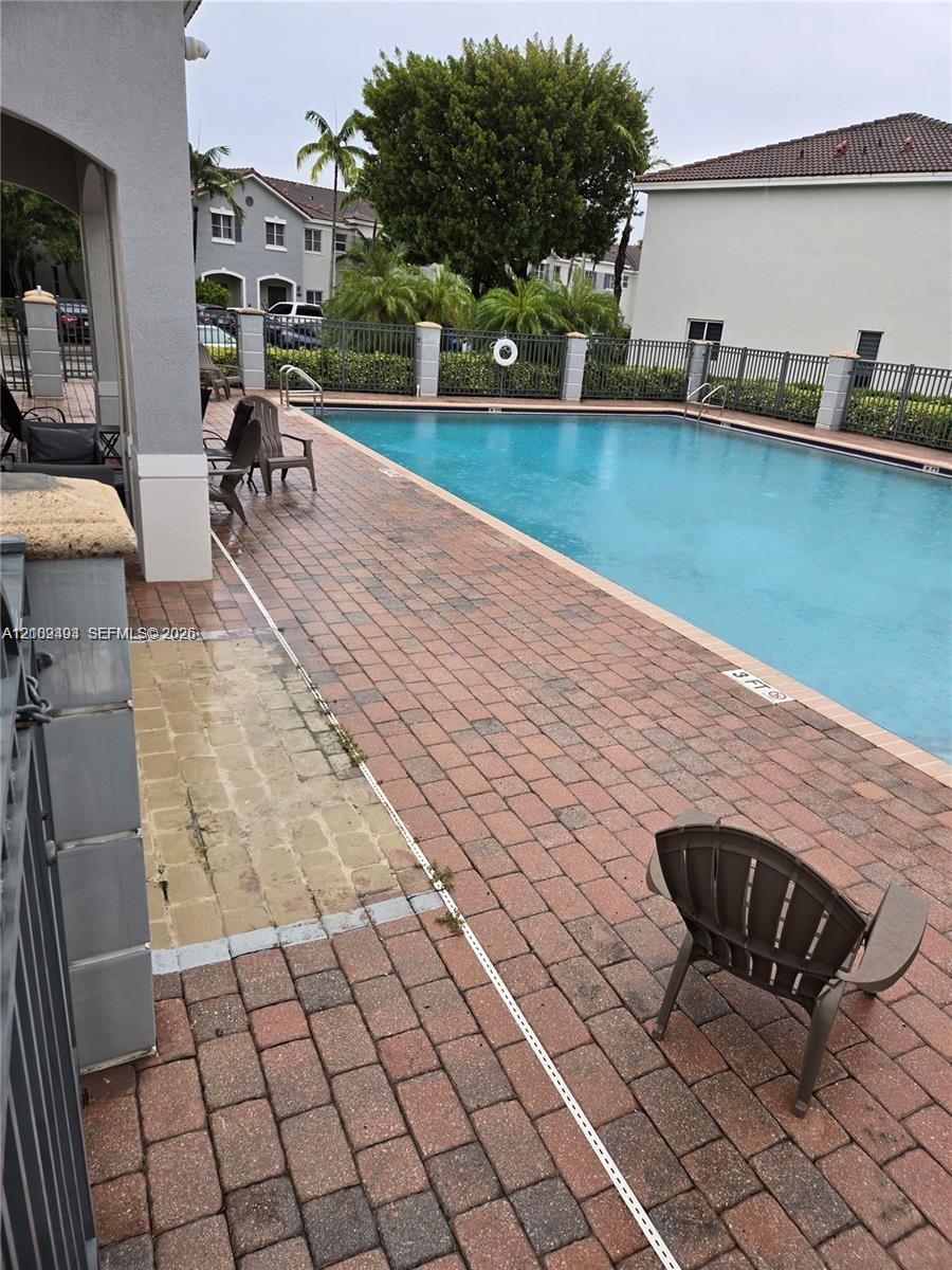 Rectangular swimming pool featuring brick paver decking, decorative metal fencing, and stone-capped perimeter pillars
