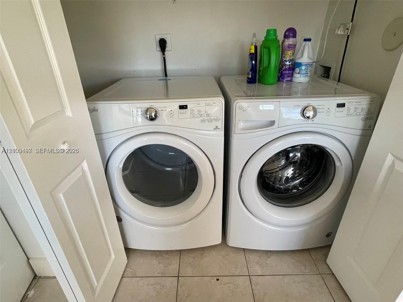 Laundry closet featuring dual white front-load appliances and neutral floor tiling