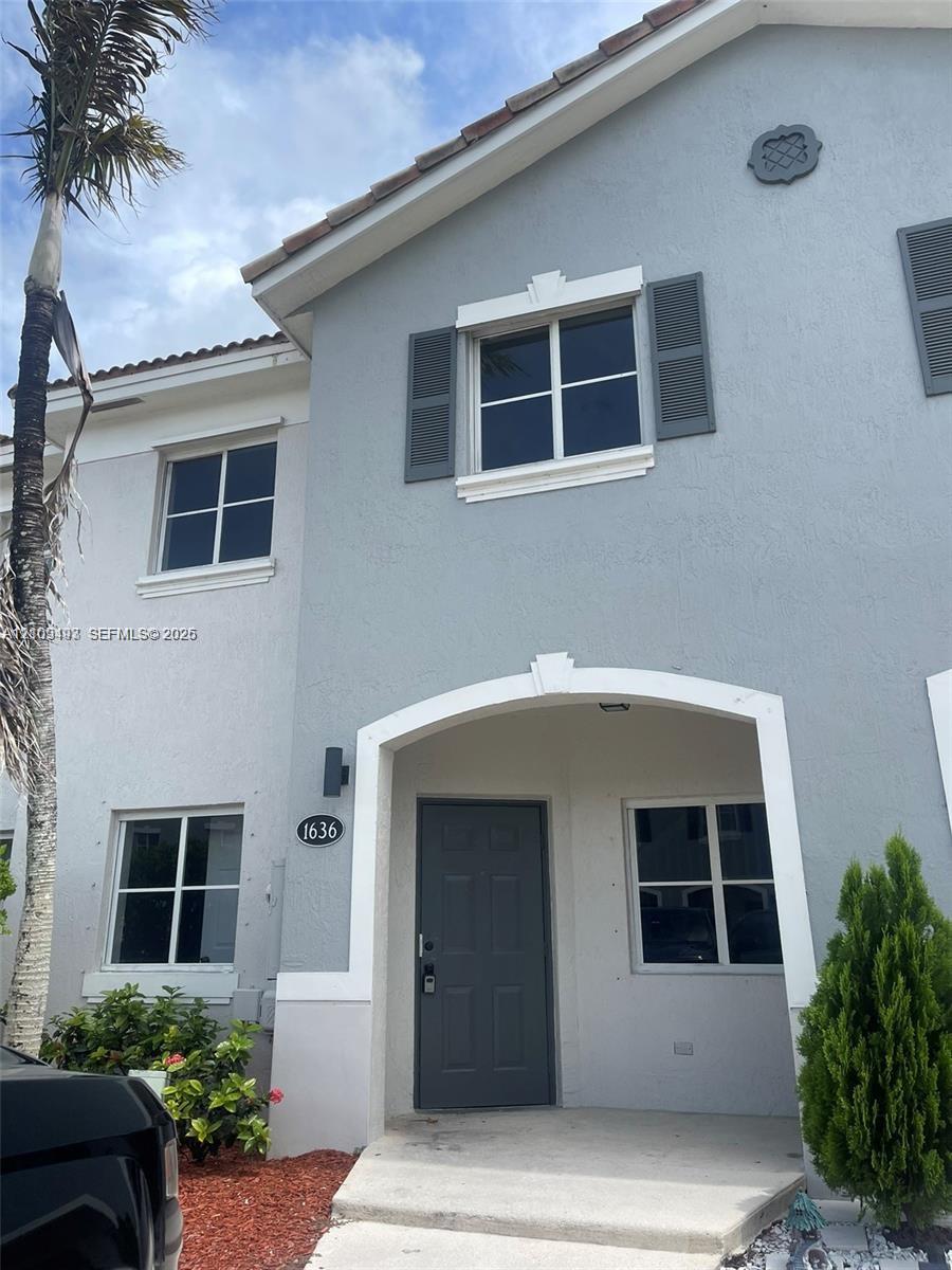 Exterior featuring a light-toned stucco facade, arched entryway, decorative window shutters, and a covered porch