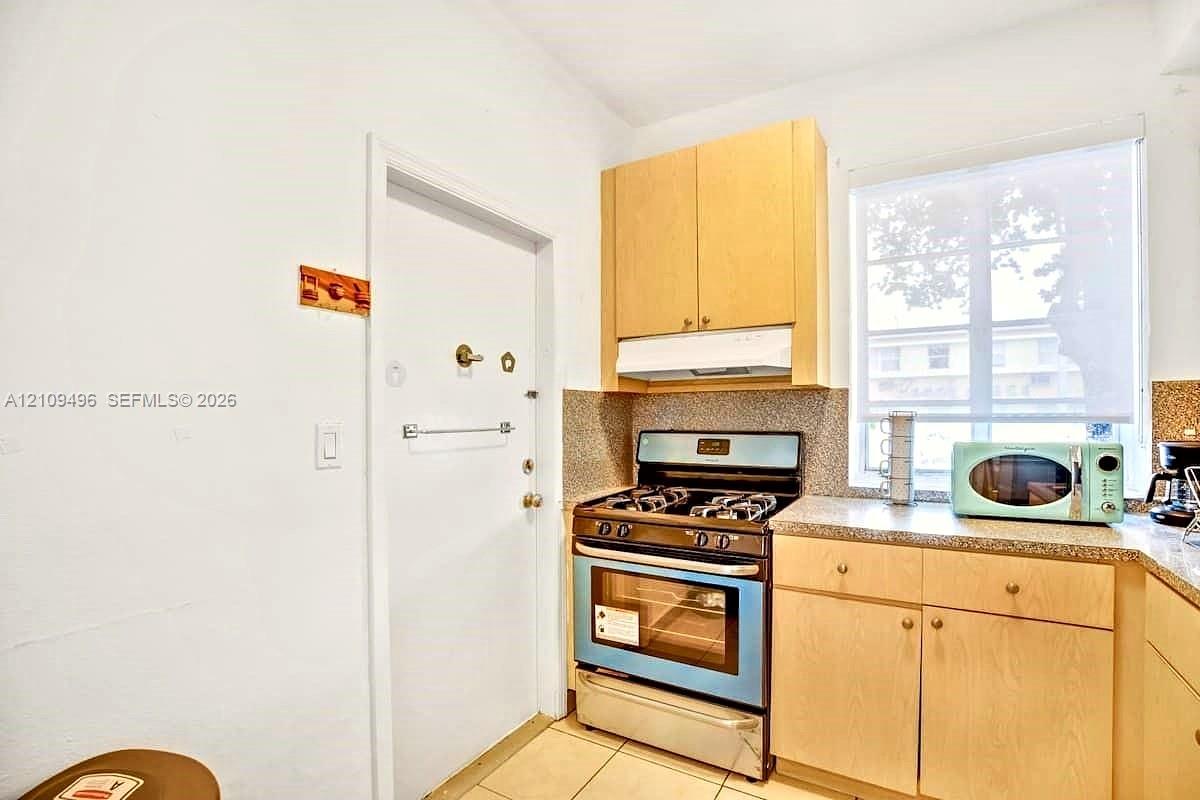 Kitchen featuring light wood-finish cabinetry, a gas range with an integrated oven, stone-patterned countertops, and a large window