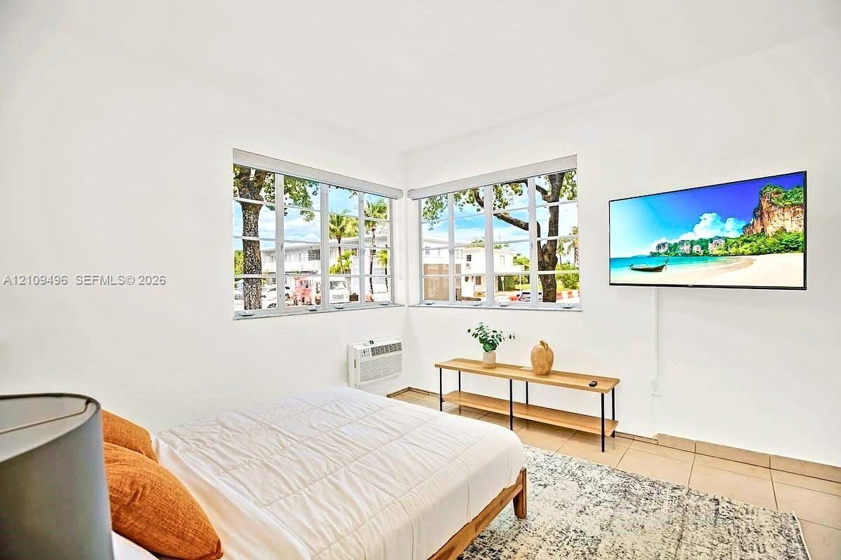 Corner room featuring large paneled windows, neutral wall-to-wall tile flooring, and a wall-mounted unit for climate control