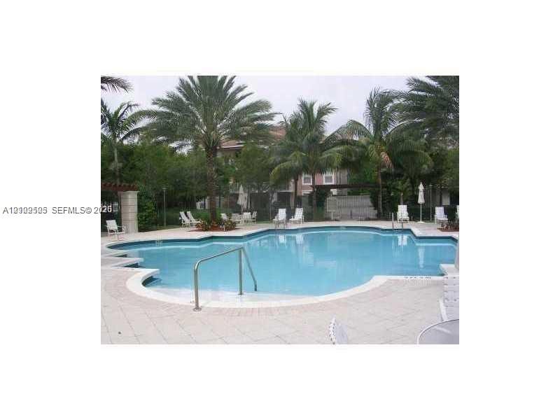 In-ground swimming pool featuring a curved design, metal handrail, concrete paver decking, and surrounding mature palm trees