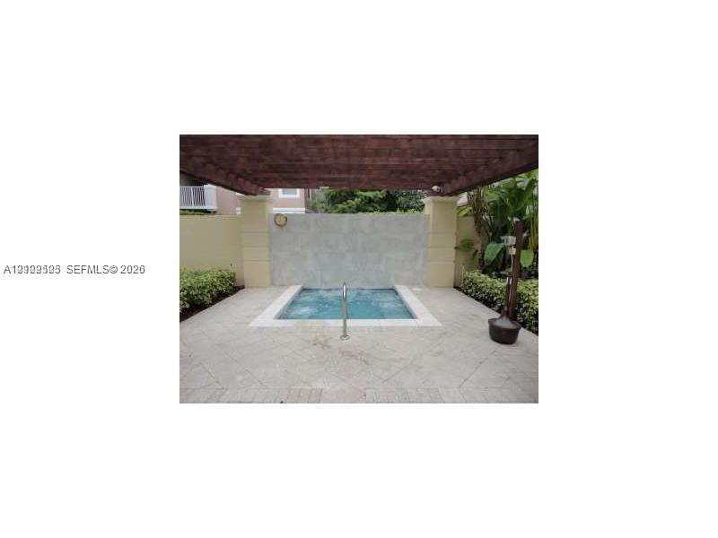 In-ground spa featuring a stone water feature, wood-slat pergola, paved patio surround, and privacy wall